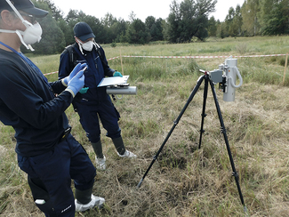 Zwei Mitarbeiter des BfS stehen während einer Messung neben einem ODL Messgerät, das auf einem Stativ befestigt ist. (Bild anzeigen)