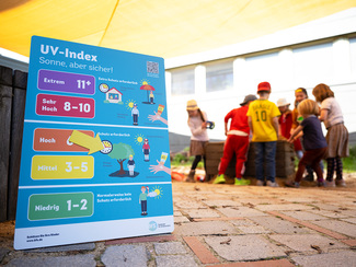 UV-Index-Magnettafel auf dem Hof, im Hintergrund eine Kindergruppe