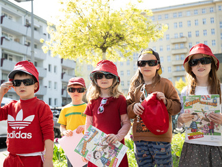 Kinder, die sich mit Kopfbedeckungen sowie Sonnenbrillen gegen die Sonne schützen und Lehrmaterialien des BfS in der Hand halten